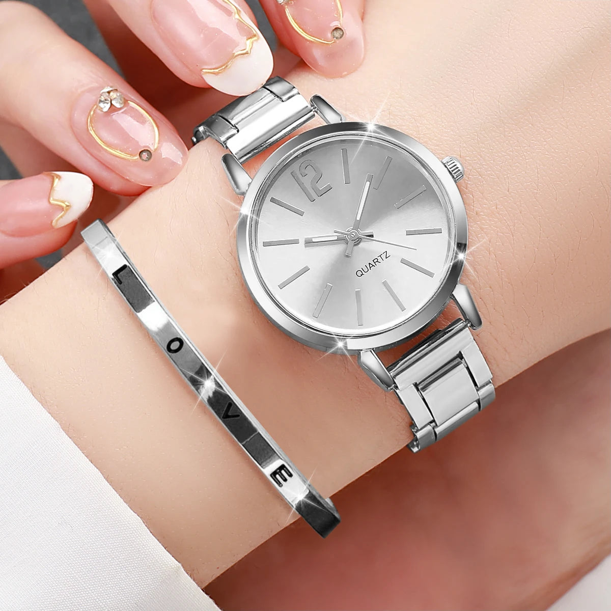 A woman's wrist wearing a gold-colored stainless steel band watch with a white dial and the text 'LOVE' on the bracelet.