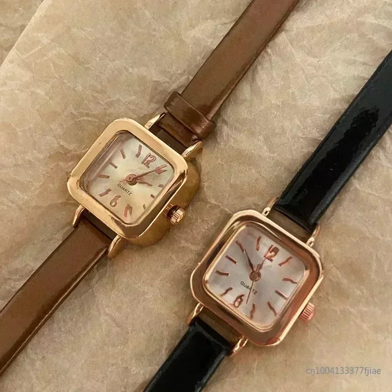 Two women's wristwatches with small square dials, one with a brown leather strap and gold case, and the other with a black leather strap and gold case.