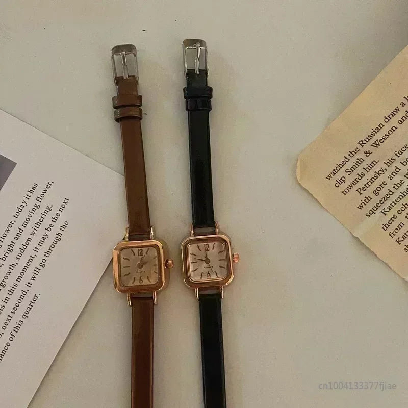 Two women's wristwatches with small square dials, one with a brown leather strap and gold case, and the other with a black leather strap and gold case.