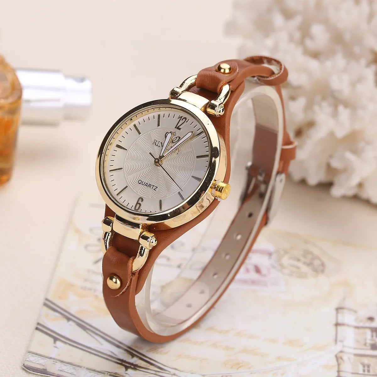 A women's quartz watch with a round silver dial and a brown PU leather strap, displayed on a mannequin wrist.