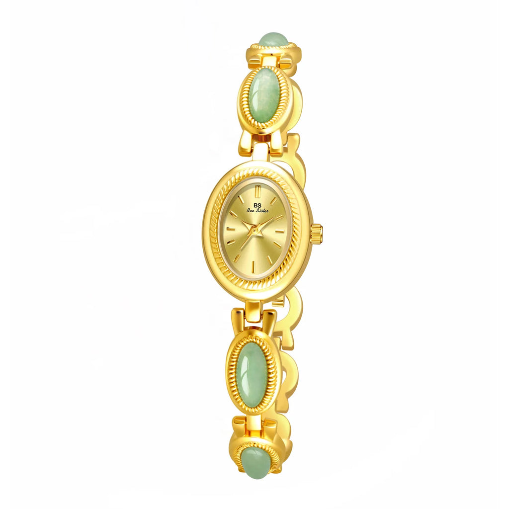 A woman's wristwatch with a gold case and green stone accents on the bracelet, displayed on a person's wrist.