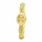A woman's wristwatch with a gold case and green stone accents on the bracelet, displayed on a person's wrist.